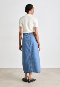 Svetlo obarvan pleten top v kombinaciji z dolgo modro denim krilo. Črne balerinke, minimalistična različica in blagovna oznaka iz usnja na krilu.