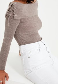 Haut marron côtelé à manches longues avec design épaules dénudées et détail à lacets sur l'épaule, associé à un pantalon blanc taille haute.