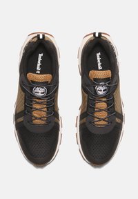 Zapatillas de malla negras y marrones con un diseño texturizado, que presentan rayas negras, un logo redondo y una suela blanca con acentos marrones.