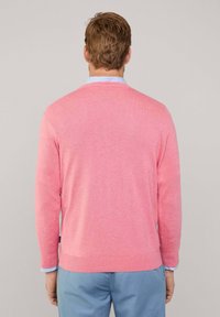 Maglione rosa chiaro, collo a giro, maniche lunghe, polsini e orlo a coste, indossato sopra una camicia a righe blu e bianche, mostrato da dietro.