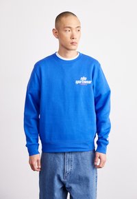 Hanorac albastru din amestec de bumbac, cu manșete și guler din material ribat. Include un logo alb Nike Sportswear pe piept.
