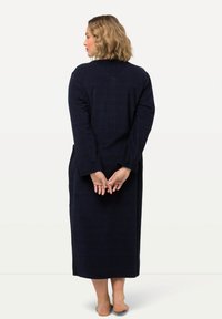 Námořnická modrá dlouhá róba s dlouhými rukávy, vyrobená z texturované látky, má rovný střih a boční kapsy, model zobrazen zezadu.