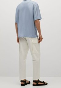 Chemise bleu clair à manches courtes, pantalon cargo blanc avec poches latérales, et sandales noires. Tissu lisse, coupe décontractée, design minimaliste.