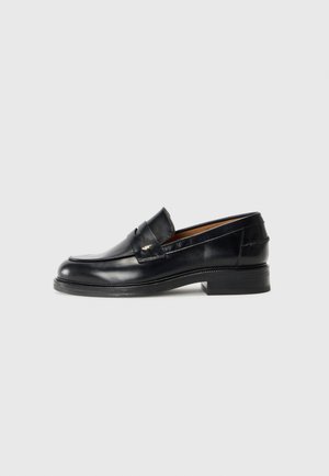 Black leather loafer with a sleek design, rounded toe, decorative strap, and a low stacked heel. Features subtle stitching and a smooth texture.
