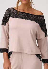 Jasnoróżowa bluzka o żebrowanej fakturze z czarną koronką wzdłuż ramion i rękawów, luźny krój i rękawy o długości trzech czwartek.