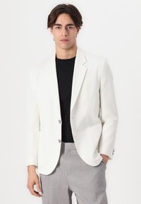 White textured blazer with notched lapels and two silver buttons, paired with a black shirt and grey trousers, presenting a tailored fit.