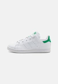 White leather sneakers with green accents and branding, featuring a low-top design, round toe, and perforated sides for ventilation.