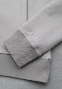 El sudadera gris presenta una combinación de tejido texturizado y suave, puños acanalados y costuras tonales sutiles. Diseño simple y limpio sin acentos adicionales.