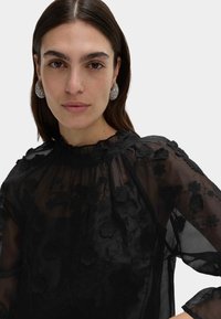 Czarna przezroczysta bluzka z kwiatowym haftem. Marszczony, wysoki kołnierz, długie rękawy z elastycznymi mankietami oraz fakturowane wzory na całej powierzchni.