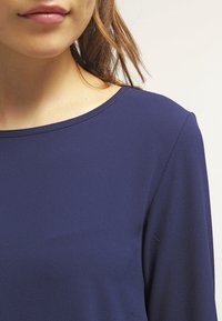 Mörkblå topp i ett mjukt, lätt material. Har en vid halsringning och långa ärmar. Strukturerad yta synlig i tygets detalj.