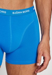 Modré bavlnené boxerky s priliehavým strihom. Majú biely pás s názvom značky "BJÖRN BORG." Hladký povrch a žiadne vzory.
