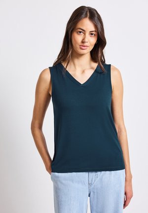 Haut sans manches en teal avec un décolleté en V en tissu lisse. Présente une coupe décontractée avec des fentes sur les côtés, associé à un jean en denim bleu clair.