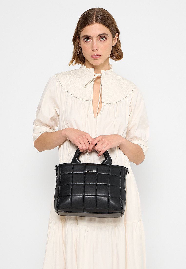Schwarze gesteppte Handtasche mit zwei oberen Griffen, glatter Lederstruktur und einem Reißverschluss. Sie verfügt über ein markiertes Metall-Accessoire auf der Vorderseite.