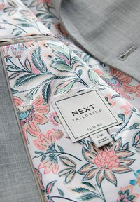 Floral gemustertes Futter in Pastellfarben mit dem Aufnäher "NEXT Tailoring Slim Fit 40R" innen am hellgrauen Sakko angenäht.