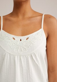 White, sleeveless top with a textured fabric, featuring floral embroidery and cutout details on the chest area, and gathered design.