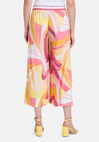 Spodnie z szerokimi nogawkami wykonane z lekkiego materiału, z wielokolorowym wzorem w odcieniach różu, żółci i pomarańczu. Szczegół z elastycznym paskiem w talii.