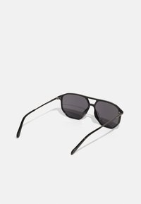 Lunettes de soleil noires avec une monture géométrique, verres gris et branches fines. Dispose d'un design moderne et d'une texture en plastique lisse.