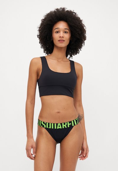 Schwarzes Bikini-Set mit einem oben kurz geschnittenen Top mit quadratischem Ausschnitt und tief geschnittenen Slips. Die Slips haben einen neongrünen Bund mit fettem Text.