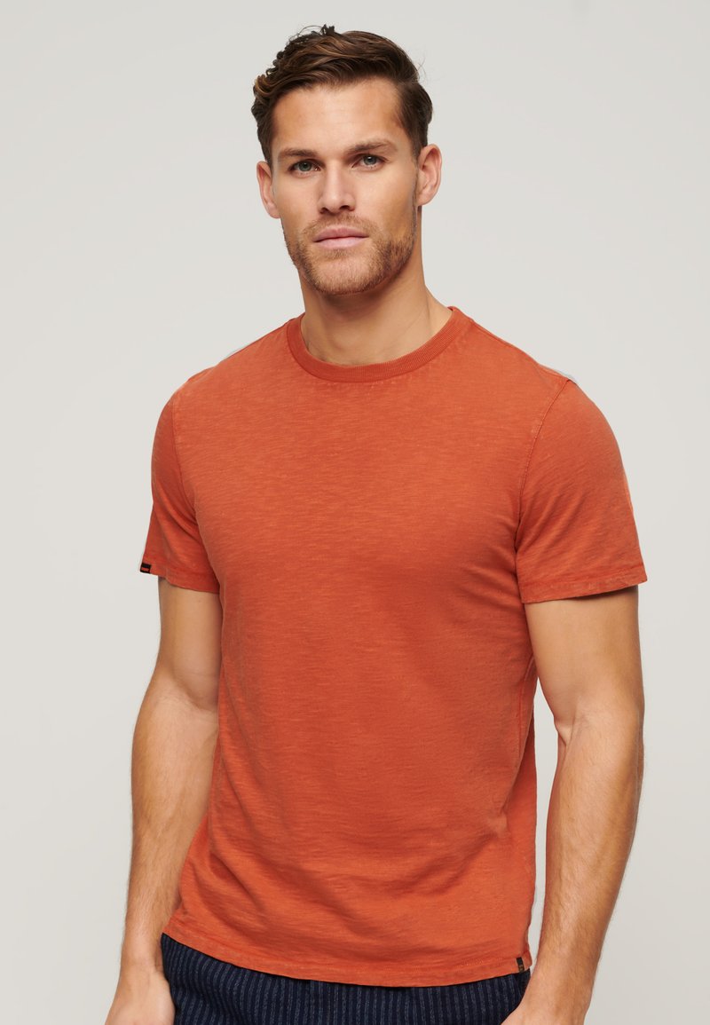 Korte mouw t-shirt met ronde hals in gebrand oranje, gemaakt van zachte stof met een licht gestructureerde afwerking en een klein accentlabel op de mouw.