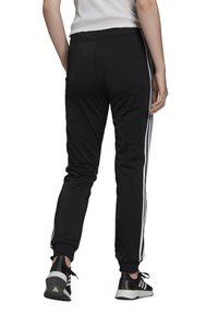 Černé sportovní tepláky s bílými pruhy po stranách, elastickým pasem a zúženými manžetami. Nošeny s černobílými teniskami.