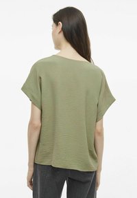 Blusa verde oliva a maniche corte in tessuto leggero e strutturato. Vestibilità rilassata con scollo a barca e spacchi laterali. Abbinata a jeans scuri.