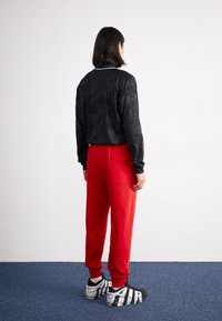 Svart kort jacka med texturerad design, tillsammans med röda sweatpants och svarta sneakers. Miljön har en enkel bakgrund och blå matta.