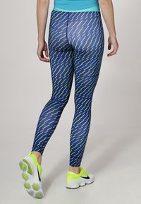 Leggings aderenti con una base blu e linee diagonali verdi e azzurro chiaro. Presentano una texture liscia e un elastico in vita.