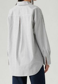 Chemise à boutons rayée blanche et noire avec manches longues, un pli au dos et un ourlet arrondi. Confectionnée dans un tissu léger avec une coupe décontractée.