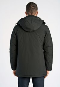 Mörk puffjacka med huva, har en slät textur och dragkedja framtill. Bakdelen har en något längre skärning och sidofickor.