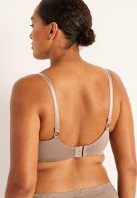 Vaaleanbeige rintaliivit, joissa on säädettävät satiinivetimet, koukku- ja silmäkiinnitys sekä sileä kangas. Viimeistelty hienolla pitsireunuksella vyötäröllä.