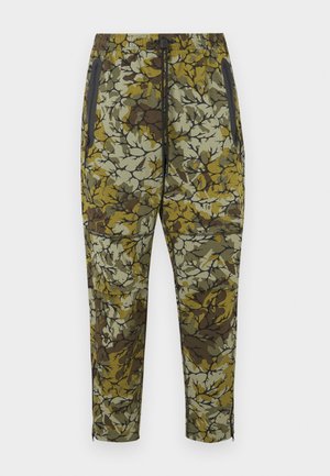 Pantalones de camuflaje en verde, marrón y beige. Con cinturilla elástica, bolsillos laterales con cremallera y ajuste cónico con cremalleras en los tobillos.