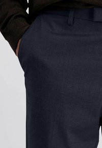 Donkerblauwe broek van een soepele, gestructureerde stof. Heeft een zijzak en een rechte snit. Gecombineerd met een donkere, gebreide trui.