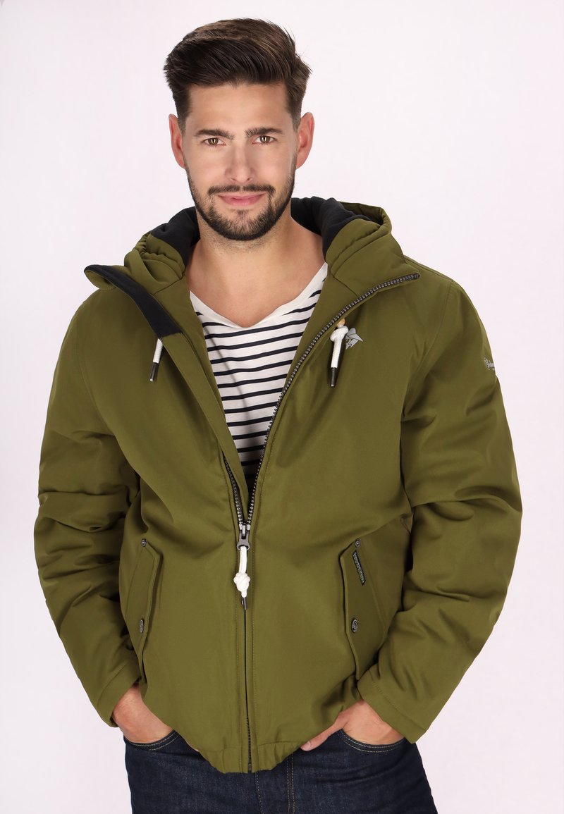 Giacca a vento color verde oliva con cappuccio e zip frontale, dotata di due tasche laterali, cordini regolabili e dettagli neri sul cappuccio e sul colletto.