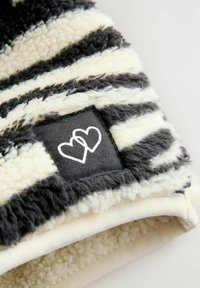 Schwarz- und cremefarbener gestreifter Fleece-Pullover mit einer weichen Textur. Mit einem schwarzen Etikett, das zwei weiße Herzumrisse zeigt.
