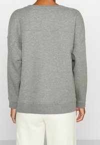Maglione grigio in tessuto morbido, con collo tondo, spalle scese e polsini e orlo a coste. La vista dal retro mostra dettagli di design minimi.