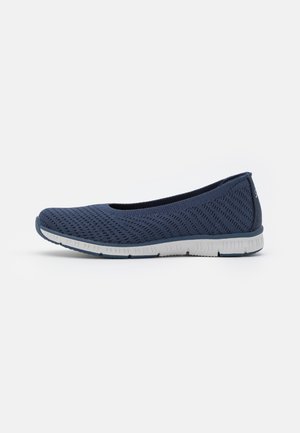 Zapato plano azul marino sin cordones con parte superior de punto y suela blanca flexible, mostrado sobre un fondo claro y liso.