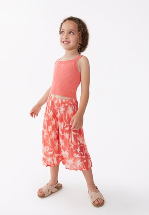 Top corto de punto color coral con patrón de chevron, combinado con una falda plisada floral que fluye en tonos coral y rosa, y sandalias beige.