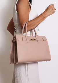 Borsa a tracolla in pelle rosa chiaro con design strutturato, manici superiori doppi e dettagli in metallo dorato. Superficie texturizzata con fondo piatto.
