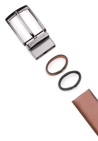 Srebrna klamra metalowa w kształcie prostokąta, połączona z dwoma bransoletkami, jedną skórzaną brązową i jedną gumową czarną, a także z brązowym skórzanym paskiem.