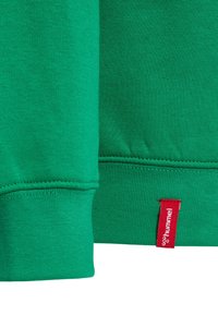 Grön sweatshirt-tyg med ribbade ärmslut och fåll, med en liten röd etikett som visar "hummel." Mjuk textur, enkel design.