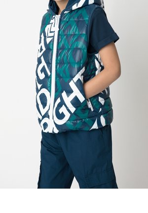 Kolorowa pikowana kamizelka z niebiesko-zielonym i białym geometrycznym wzorem, z przednim zamkiem błyskawicznym i kapturem. W komplecie z granatowymi spodniami.