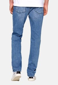 Vaqueros de mezclilla azul claro con corte recto, que incluyen dos bolsillos traseros y detalles de costura sutiles, combinados con zapatillas blancas.