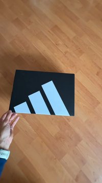 Czarne pudełko z białymi geometrycznymi paskami na górze. Pudełko jest prostokątne o matowej teksturze. Ręka podtrzymuje je od spodu.