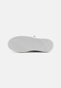 Semelle de chaussure en caoutchouc blanc avec des rainures texturées et un détail de logo. Des motifs circulaires et en vagues améliorent l'adhérence et la traction.