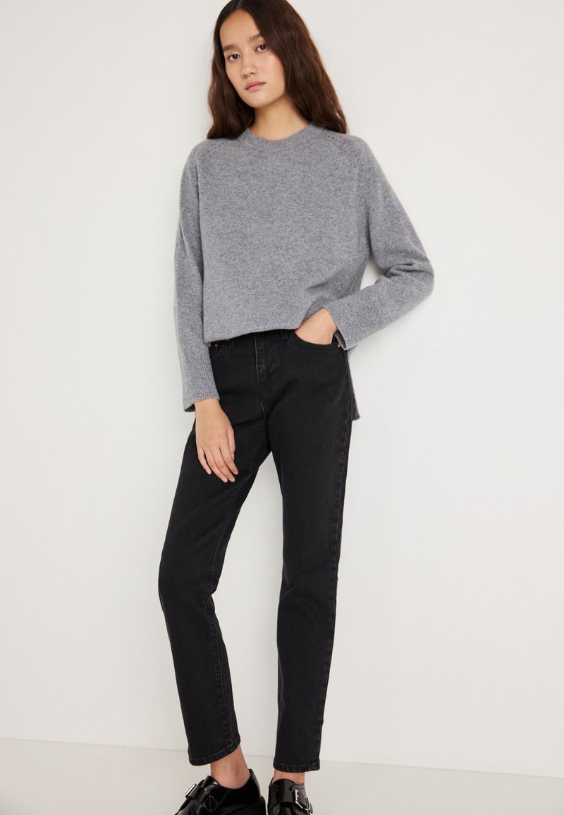 Pelēka, faktūrēta džemperis ar garām piedurknēm kopā ar augstu jostasvietu melnām džinsām. Džinsām ir taisnstūra legu dizains un priekšējas kabatas.