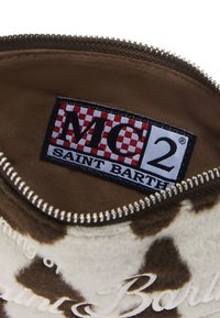 Pochette zippée en cuir de vache marron et blanc avec une texture douce. Équipée d'une étiquette de marque avec un motif à carreaux rouge et blanc.