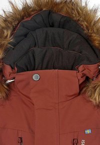 Brun isolerad jacka med huva som har svart pälsdetalj. Har en knappstängning och dragsnören, med framträdande sömnad och fickor med dragkedja.