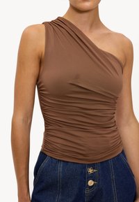 Haut brun à une épaule en tissu extensible, présentant une texture froncée le long du corsage. Associé à un short en denim taille haute.