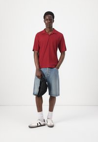 Red ribbed short-sleeve shirt, blue denim knee-length shorts, white sneakers with black accents, and a black pouch bag.