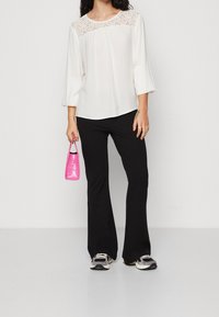 Vit blus med spetsdetaljer på oket, i kombination med svarta utsvängda byxor och en glänsande rosa handväska. Svartvita sneakers fulländar looken.